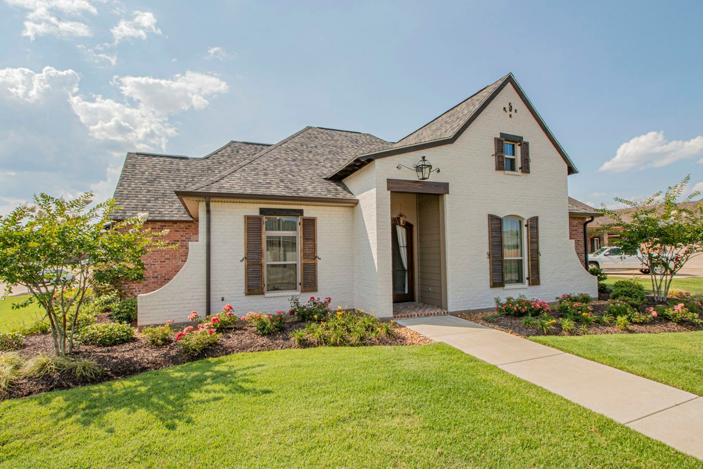 A white brick house with dark shutters, a front path, and a green lawn